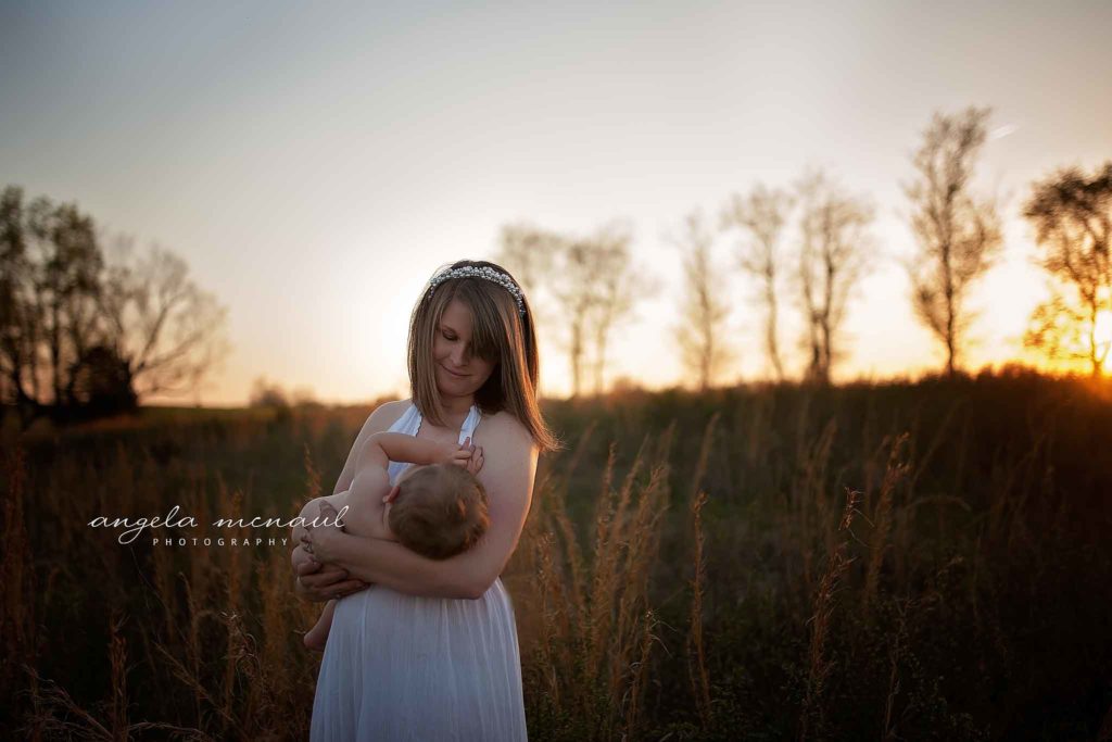 Mom in a field at sunset nursing her one year old baby