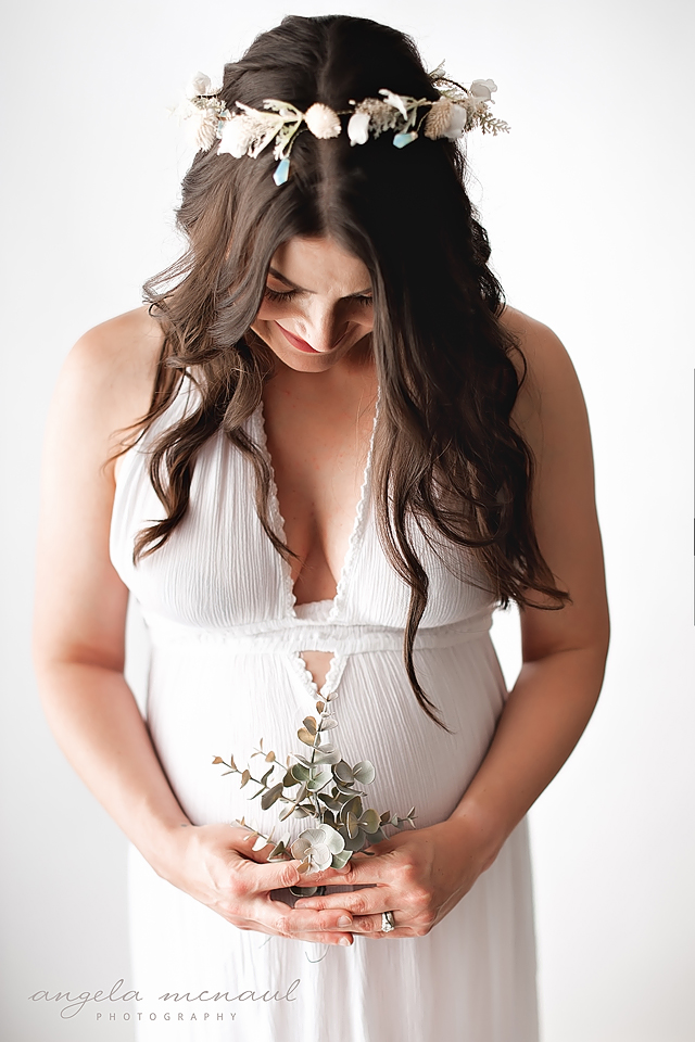 Studio Maternity photos of mom wearing white dress, holding succulents and wearing white crown
