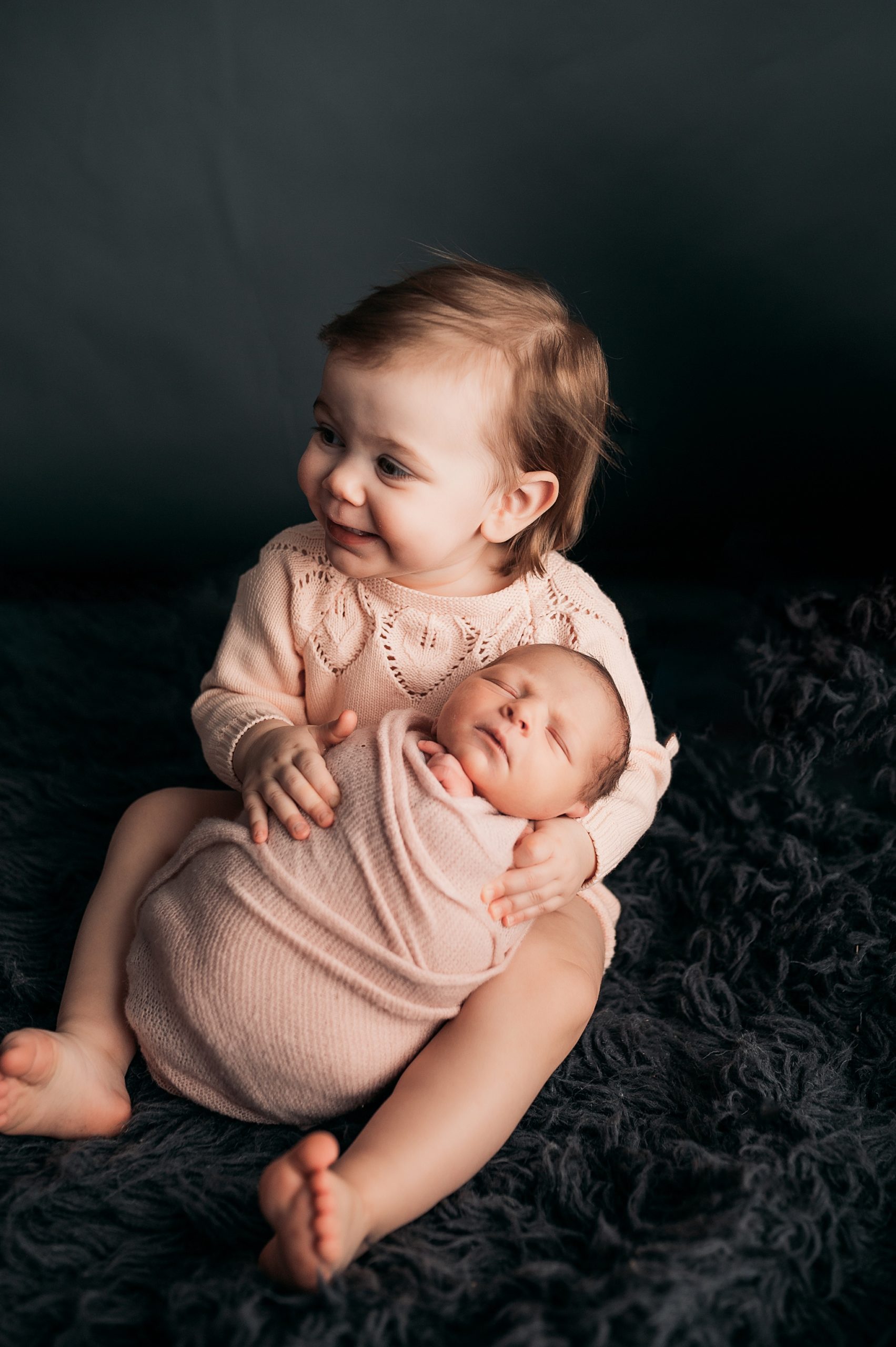 Big sister wearing pink smiling and holding newborn baby