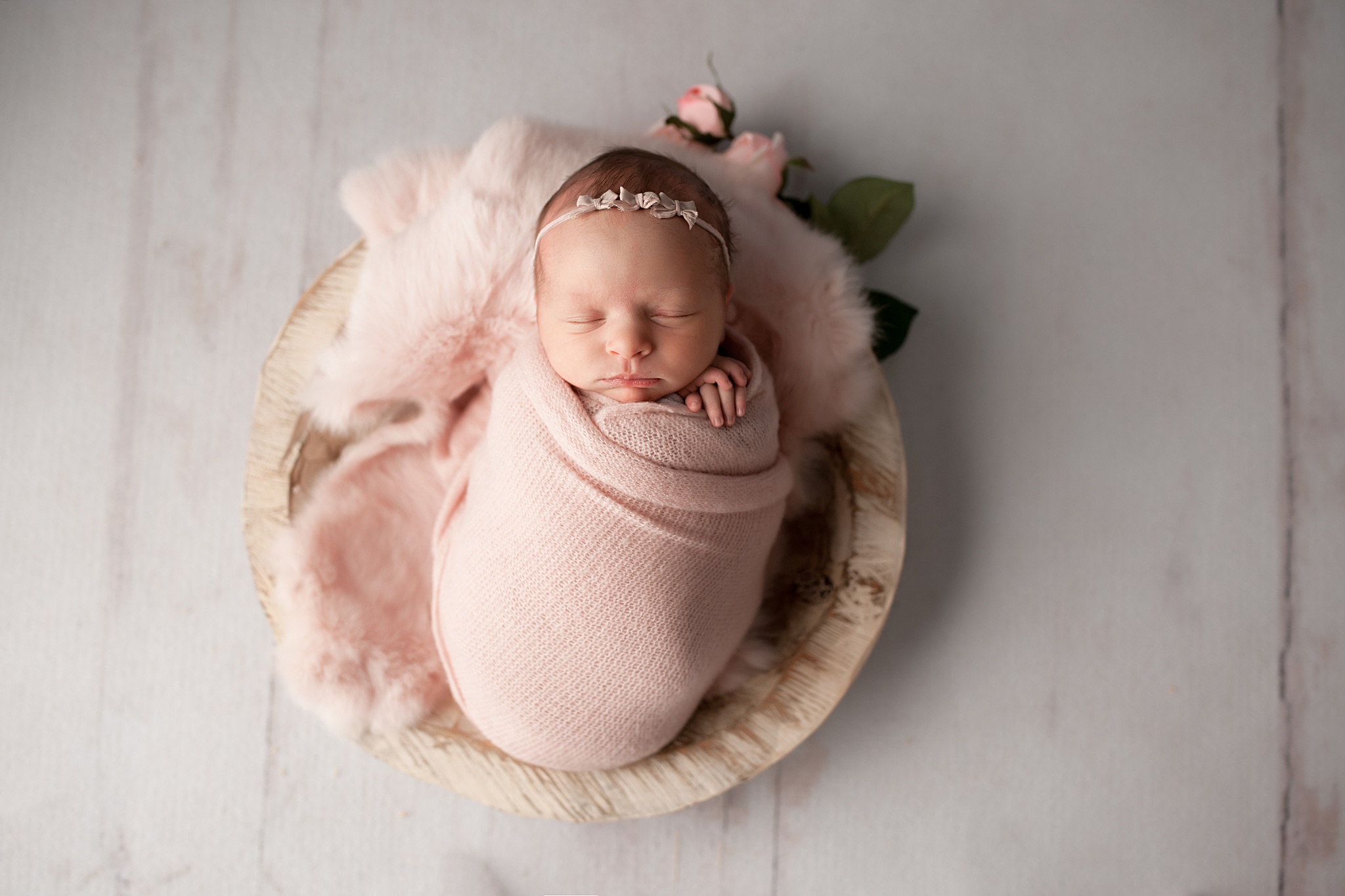 Newborn in a pink swaddle laying in a while basket