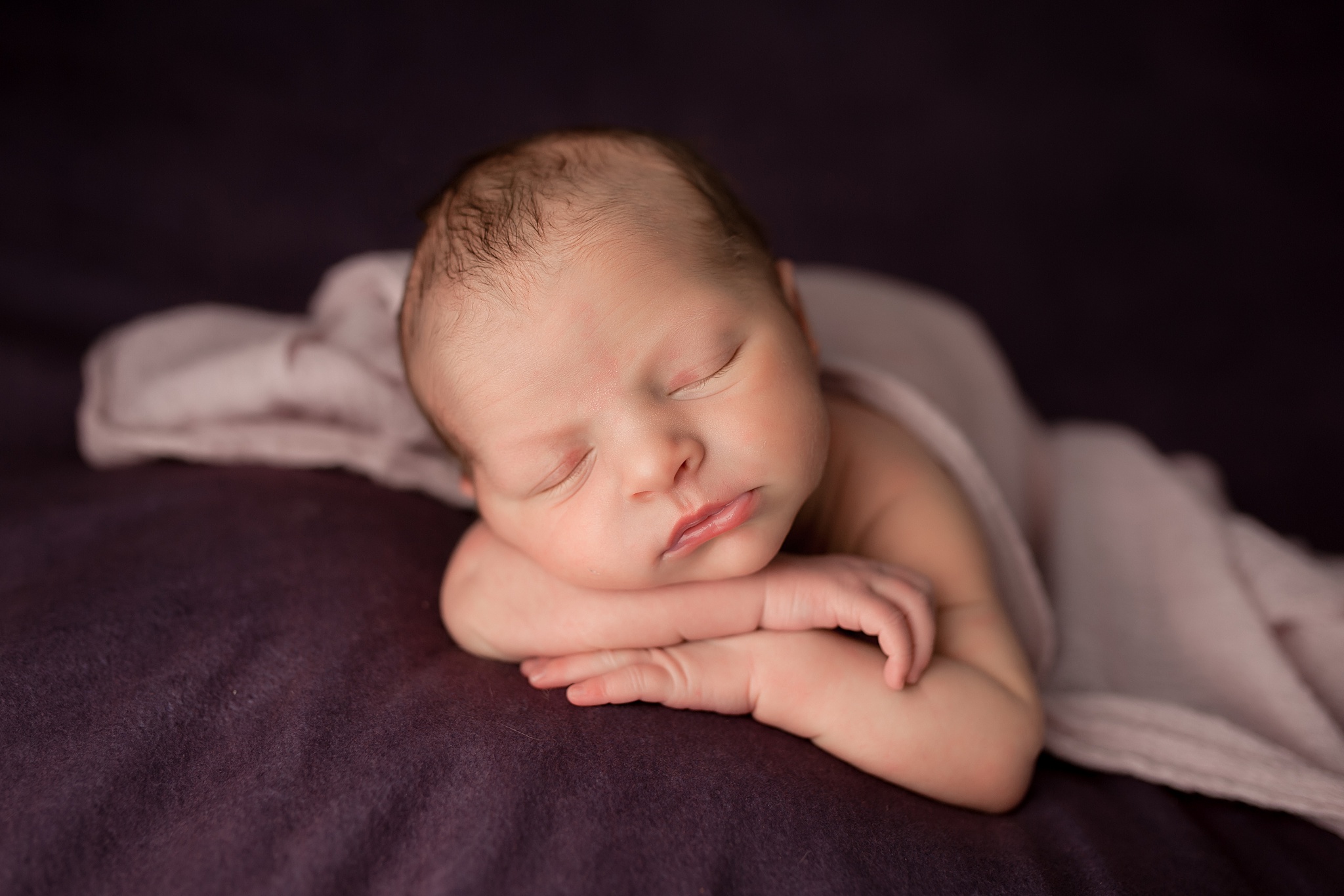 newborn in purple laying on blanket with head propped on hands