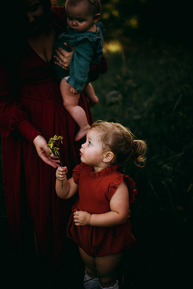 Little blond girl with a ponytail, wearing a red dress handing a bouquet of flowers to her mother