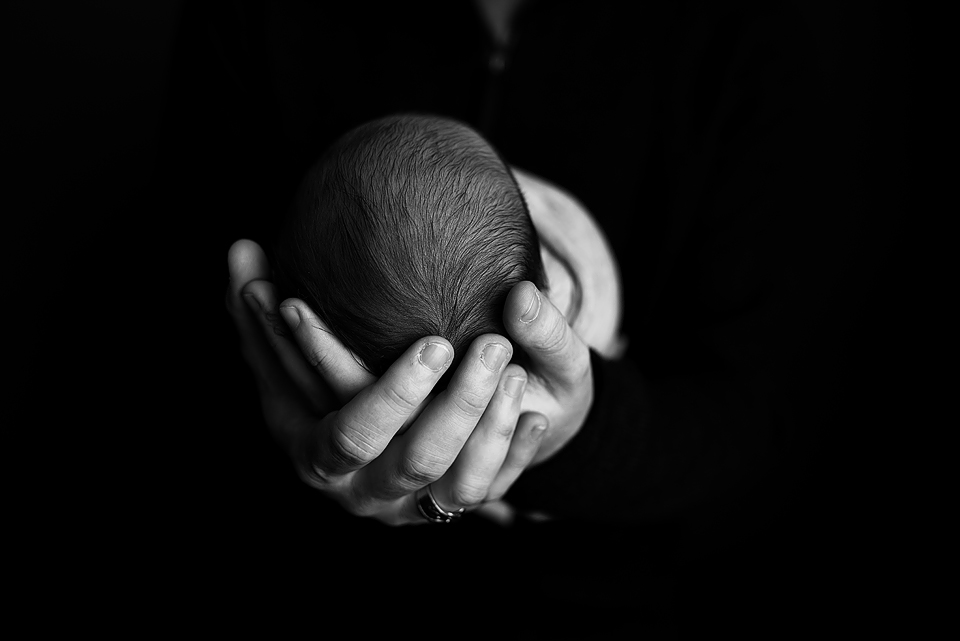 Black and White image of a newborn baby held in a pair of hands