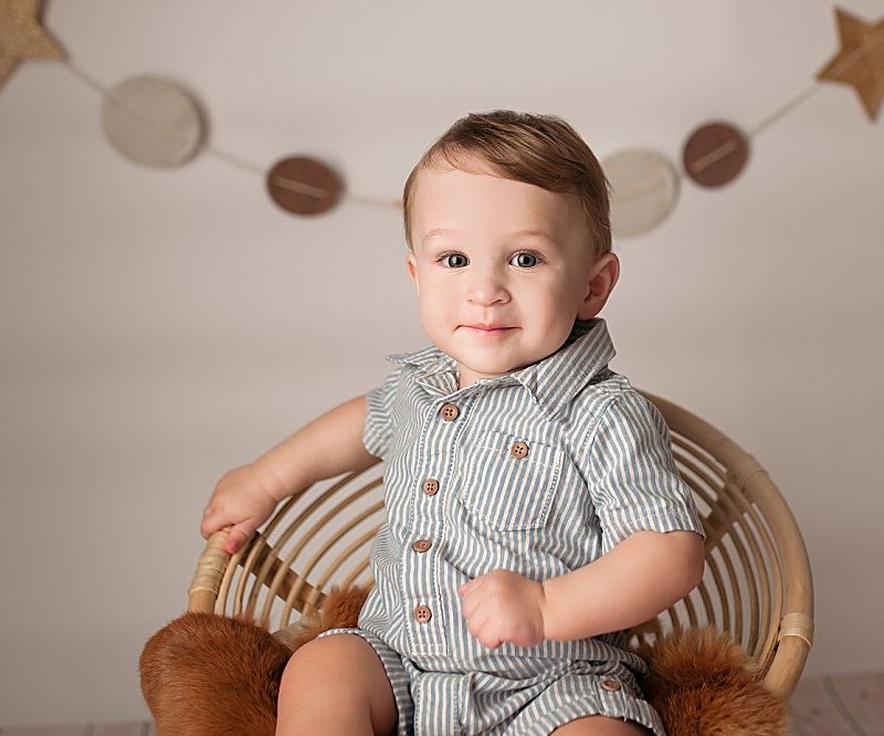baby boy sitting in papasan chair with star banner behind him