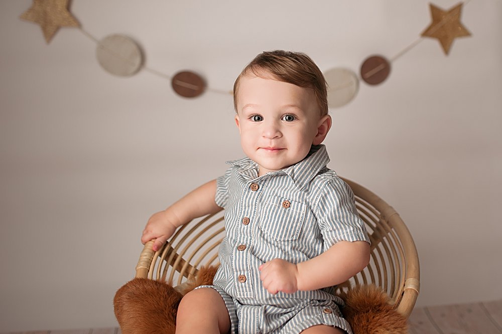 baby boy sitting in papasan chair with star banner behind him