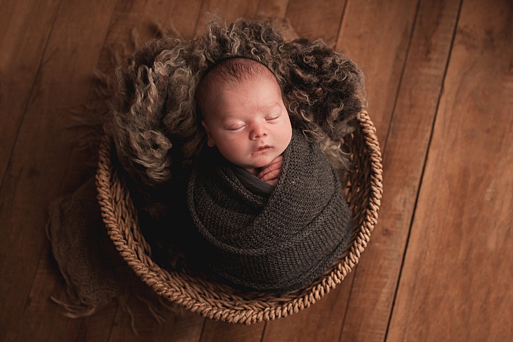 Newborn Thomas swaddled in a wrap laying in a basket