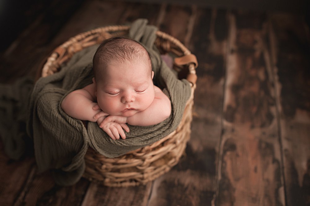 Newborn Thomas laying in a basket with his hands on his chin