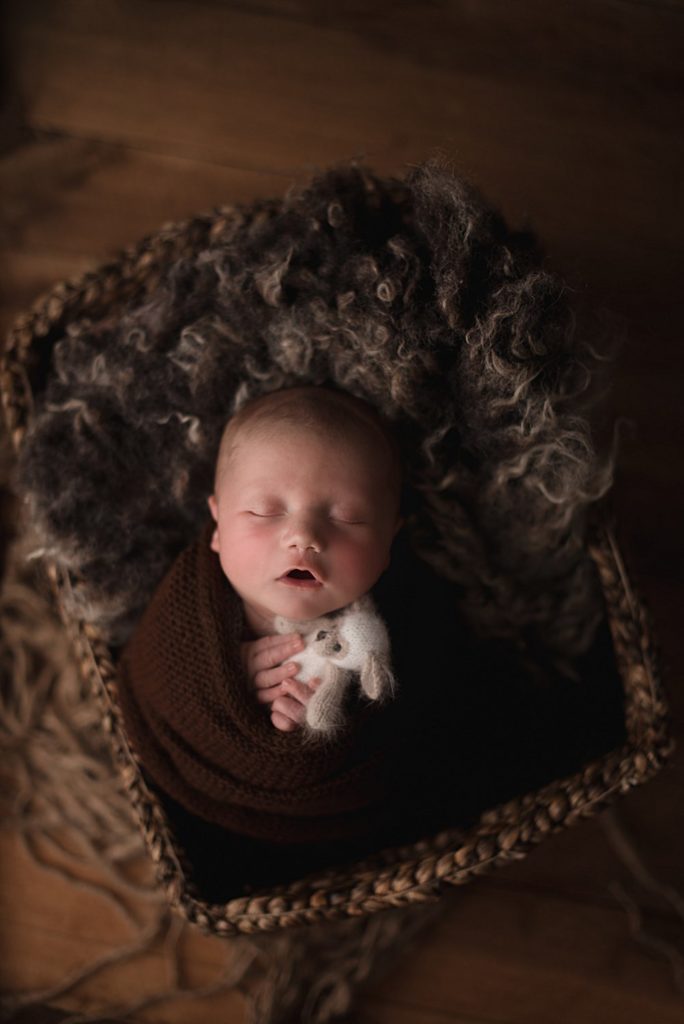 newborn sleeping with his mouth open swaddled in a brown blanket, laying in a basket
