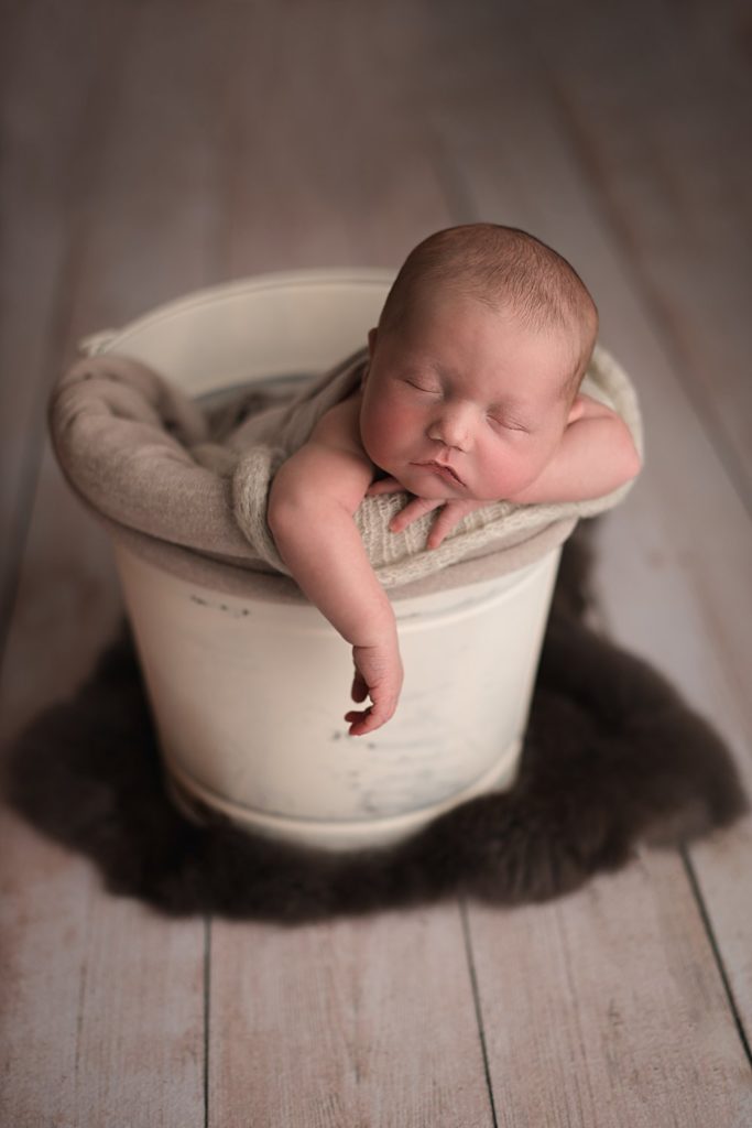newborn in a bucket with arm dangling out the side, baby is sleeping