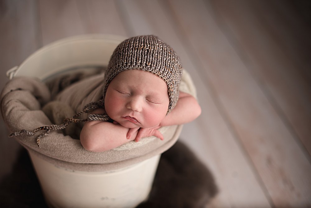 newborn in a cream bucket wearing a gray bonnet