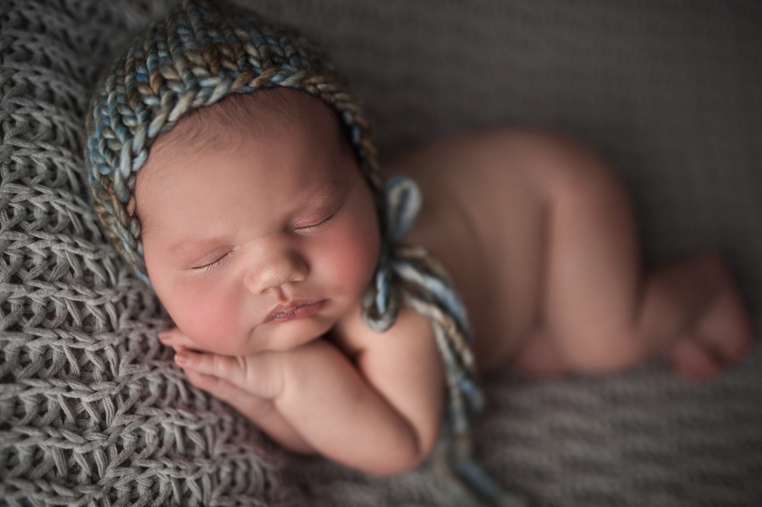 Newborn Photo of Baby laying on his side on a blue blanket with hands folded. Photographer Angela McNaul