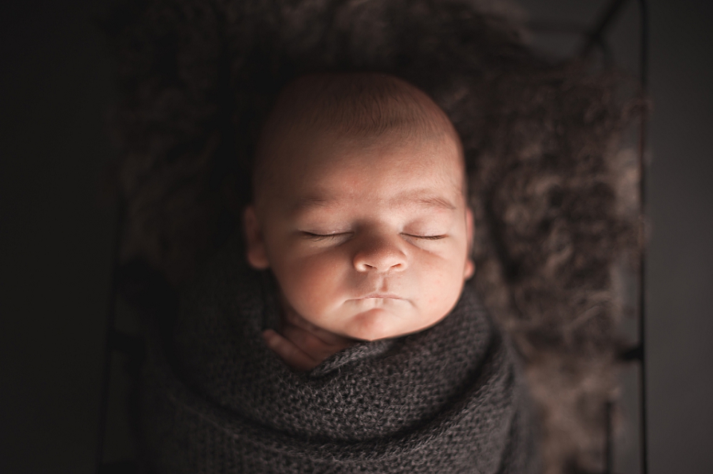 newborn baby sleeping while swaddled with grey knit wrap