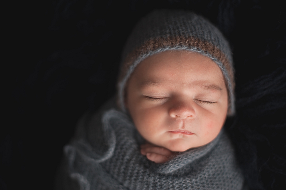 Newborn wearing blue bonnet and swaddled in blue knit wrap