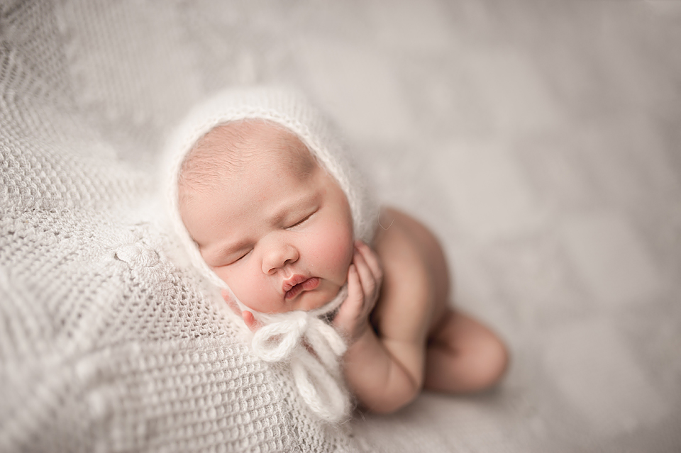 Newborn Baby Photo taken by Angela McNaul Photography girl baby in white bonnet laying on white lace blanket