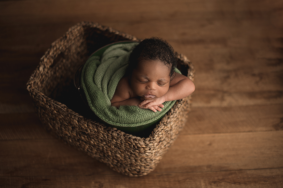 Sleeping African American Newborn baby posed in a wicker basket with a green blanket around him