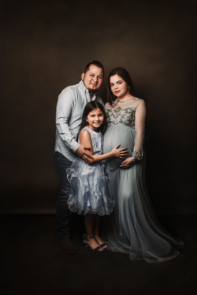 Pregnant Mom, Dad and daughter, smiling and holding pregnant belly.