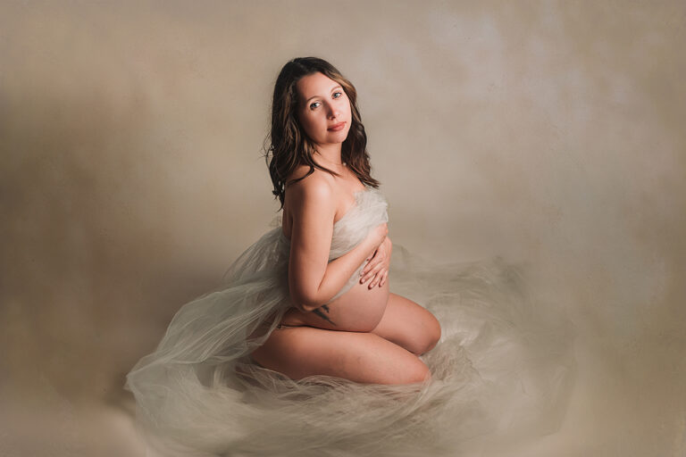 Pregnant Woman Sitting on the floor with tulle wrapped around her naked body