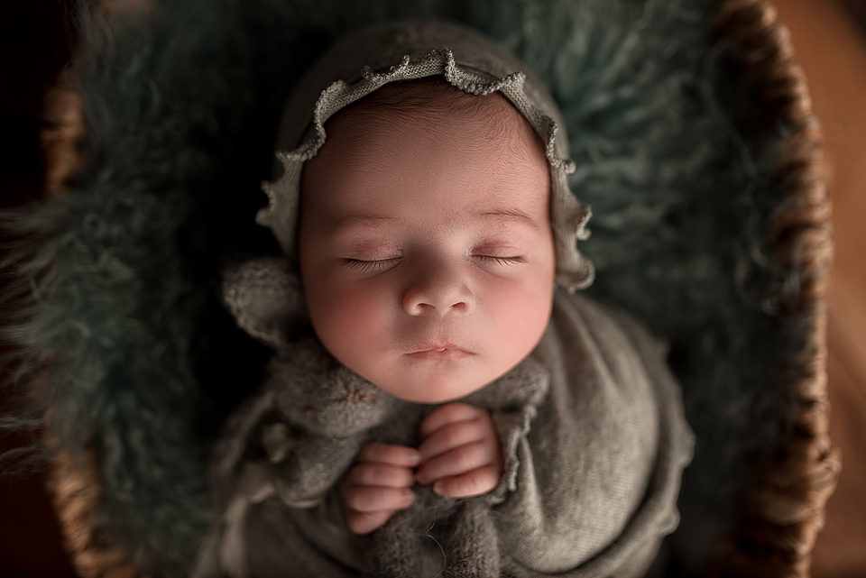 newborn baby girl holding a stuffed bunny while sleeping, wearing a ruffle trim bonnet