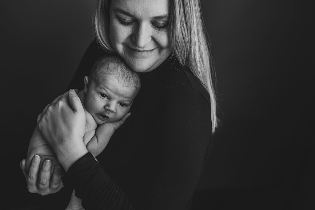 black and white photo of mom with her eyes closed holding her awake newborn baby