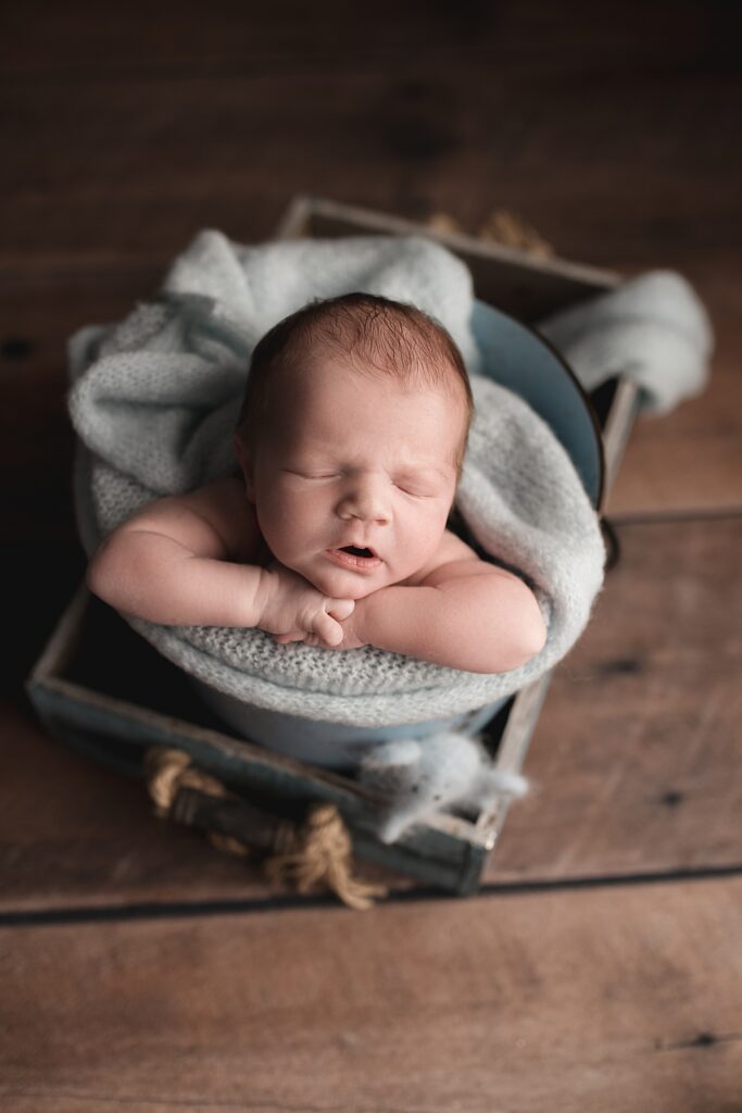 sleeping newborn baby posed in a blue bucket