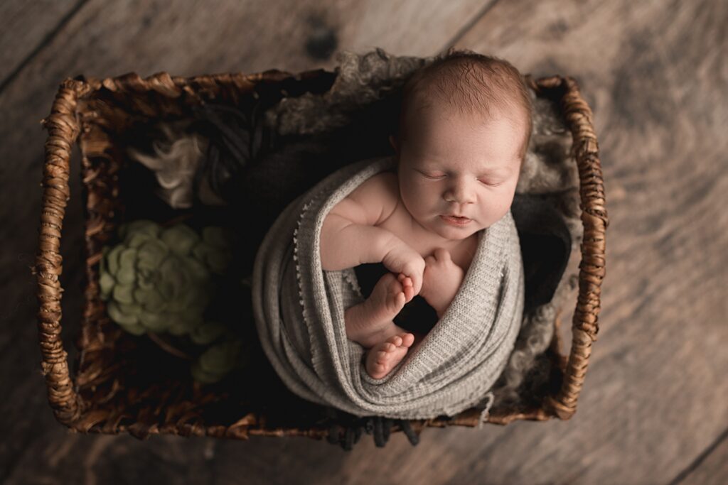 newborn sleeping in a basket with a grey wrap