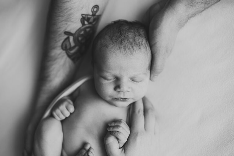 black and white photo of baby sleeping in dads arms, dad has tatoos