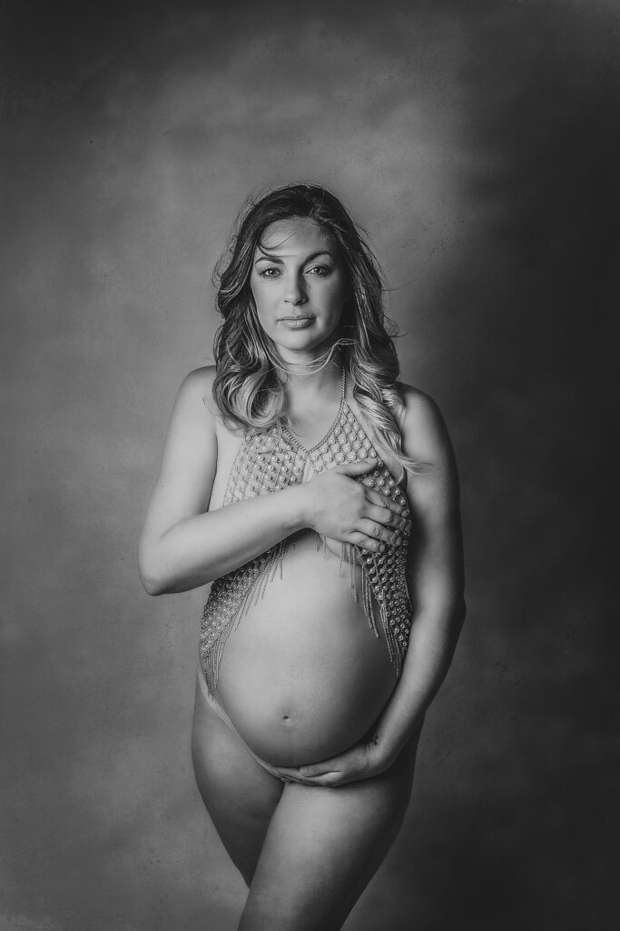 Black and white semi nude pregnant mother holding her belly while making eye contact with the viewer