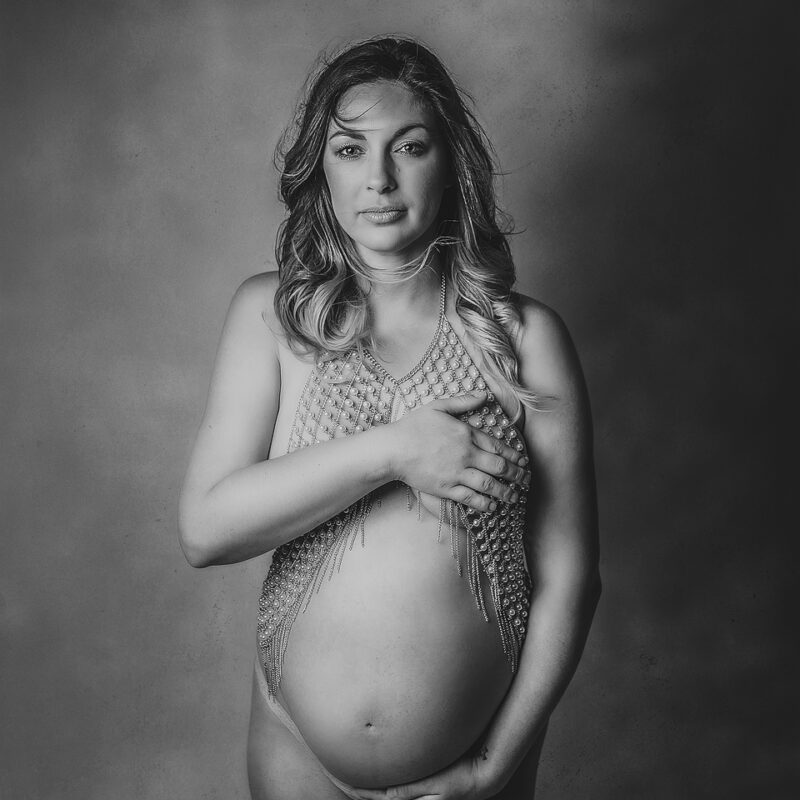 Black and white semi nude pregnant mother holding her belly while making eye contact with the viewer
