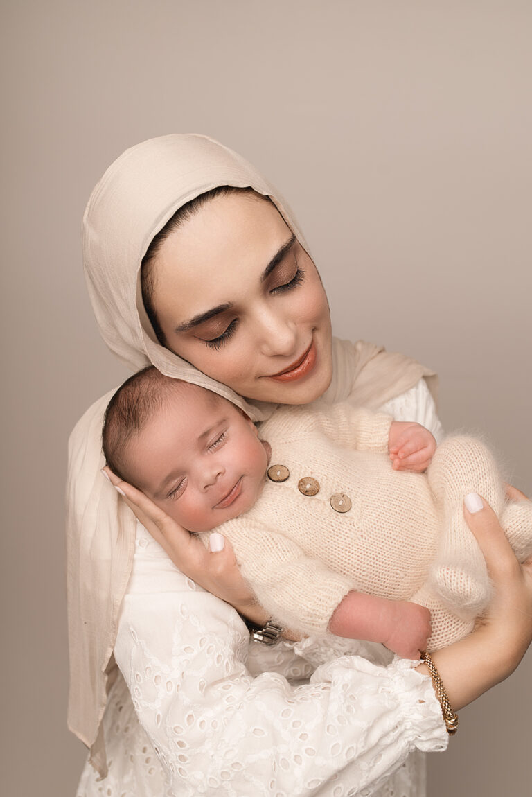 Newborn baby Zayd in parents’ arms while mother in hijab looks lovingly down at him; captured in a natural light Crozet baby photography studio