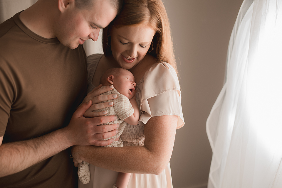 Sweet snuggles of baby in knit romper held by mom and dad