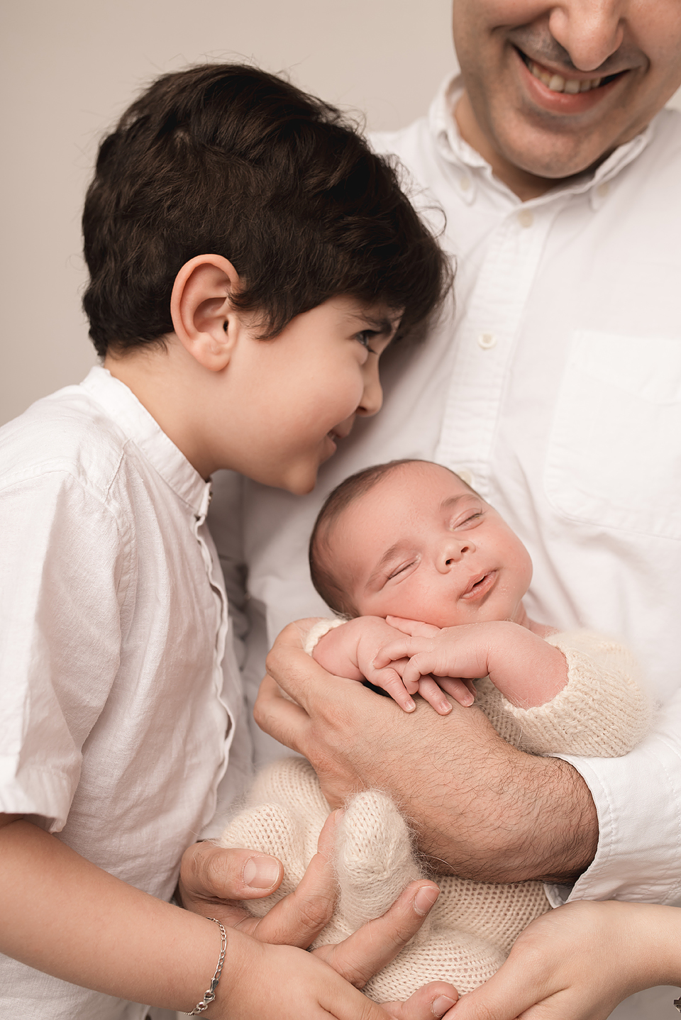 Toddler sibling laughing and kissing baby Zayd on the forehead in a softly lit newborn studio in Charlottesville.