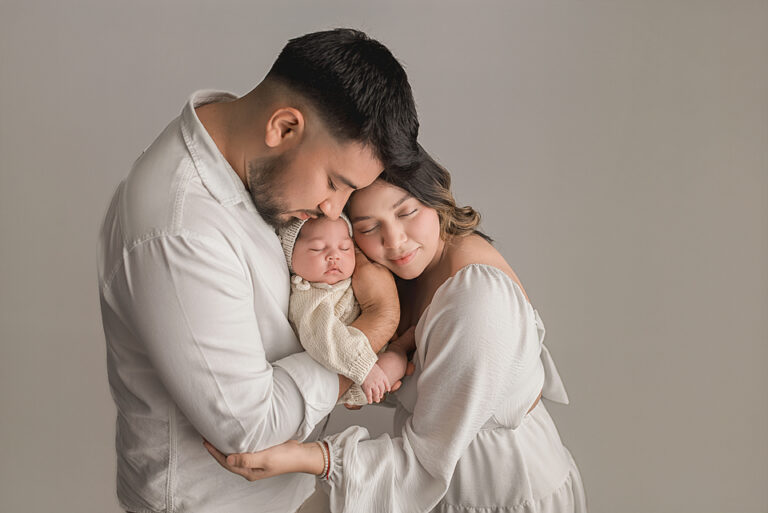 Newborn in a boho knit outfit snuggled by parents.