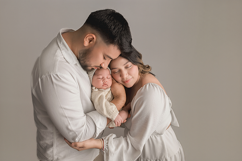 Newborn in a boho knit outfit snuggled by parents.
